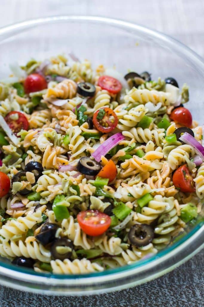 pasta salad with black olives, cherry tomatoes, red onion in a big bowl on a white board