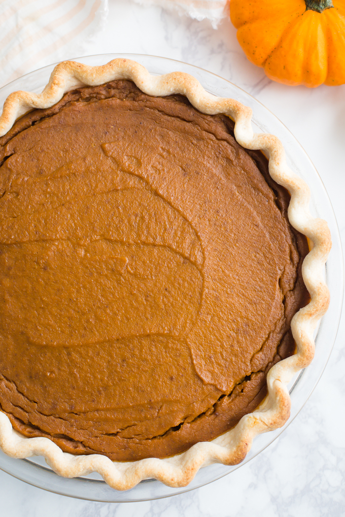 large baked pumpkin pie on a marble board with a pumpkin in the corner