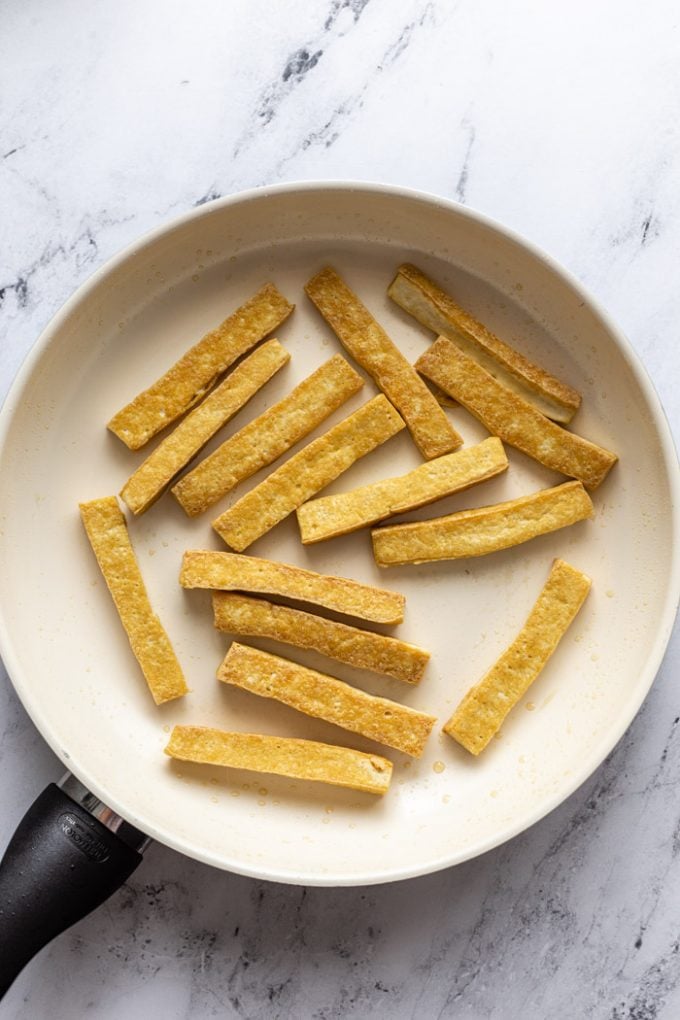 top down shot of a white skillet filled with strips of sauteed tofu