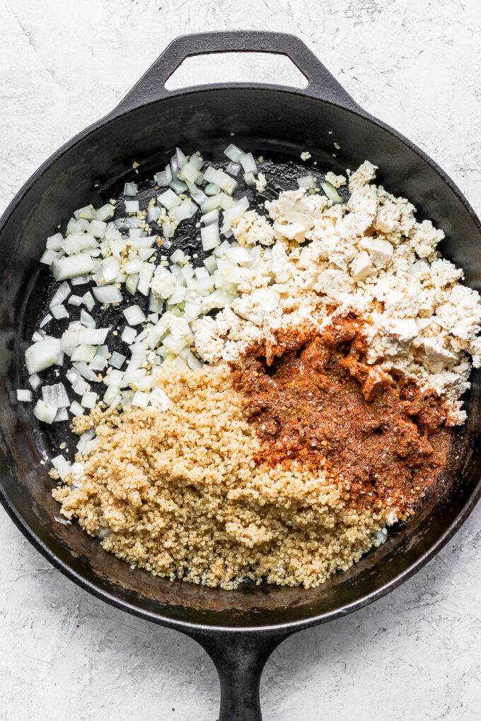 tofu taco meat ingredients in a skillet: tofu crumbles, taco seasoning, quinoa and onion