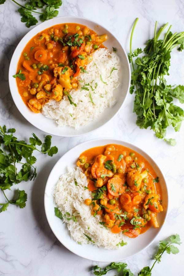 2 bowls of tikka masala and white rice on a marble background with cilantro around the bowls