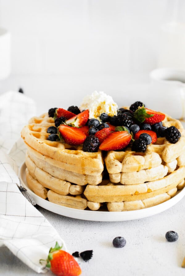 stack of vegan waffles topped with fresh berries and whipped cream