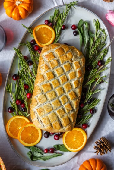 vegetarian wellington on a large platter surrounded by rosemary, orange, and fresh cranberries