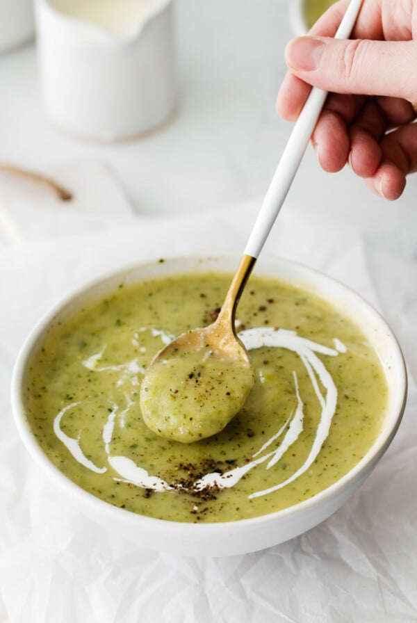 using a spoon to scoop up vegan zucchini soup out of a bowl