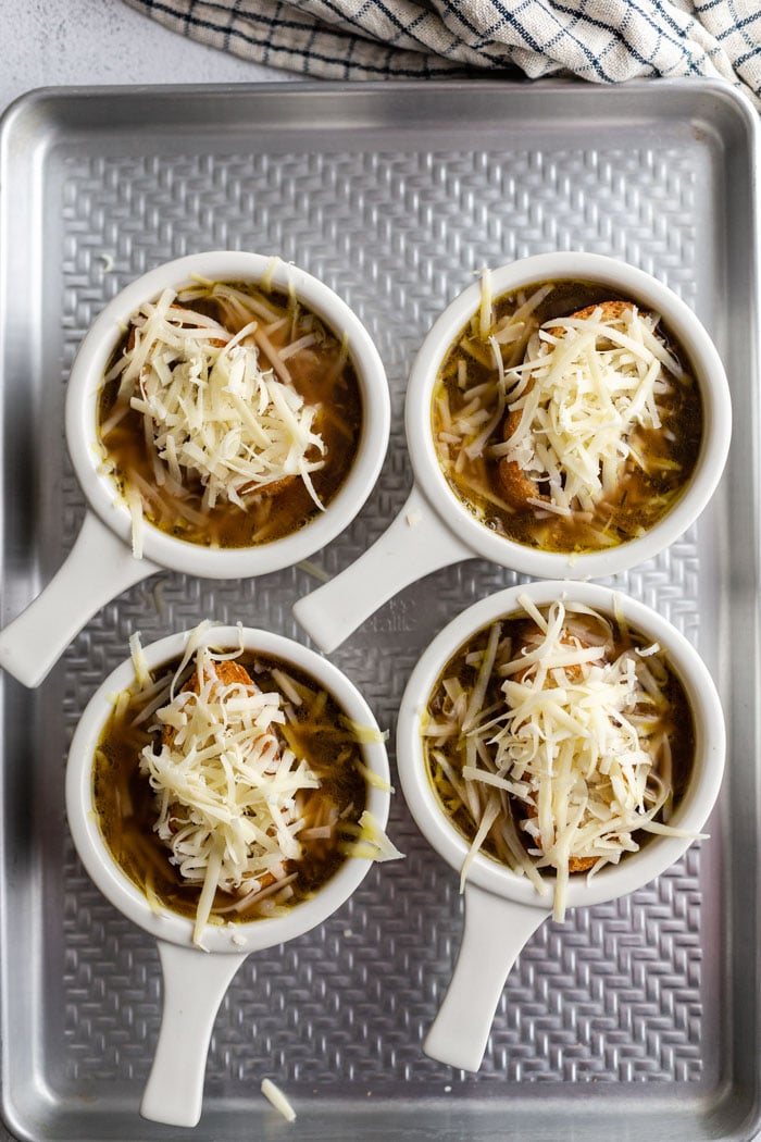 several white bowls of french onion soup with bread and cheese on top before the cheese has melted