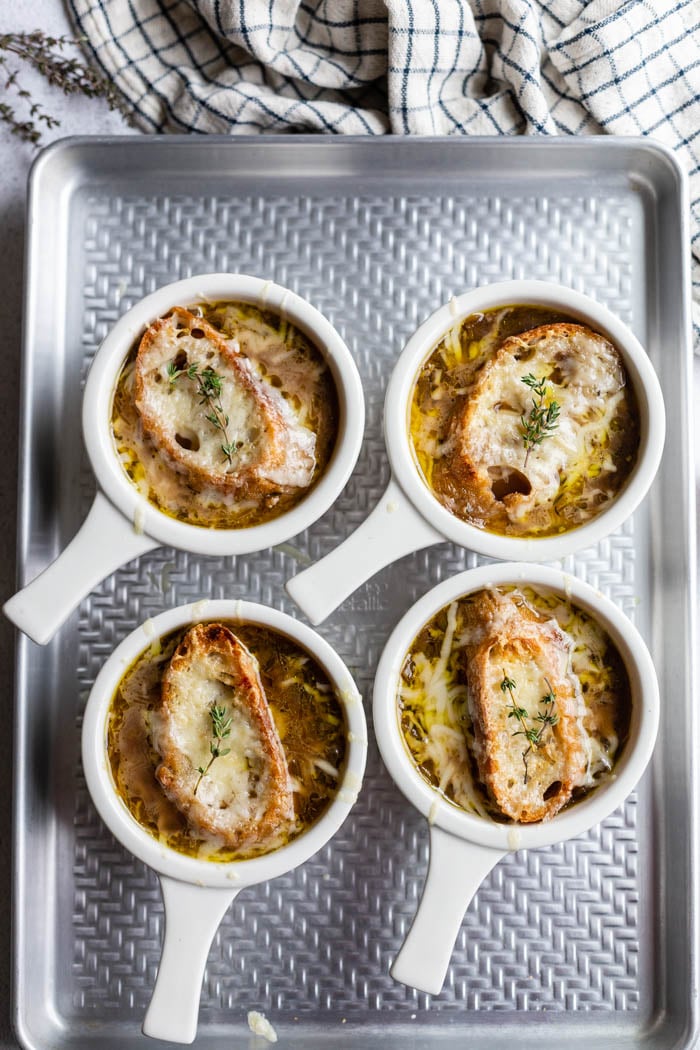 bowls of french onion soup sitting on a baking sheet with bread and melted cheese on top