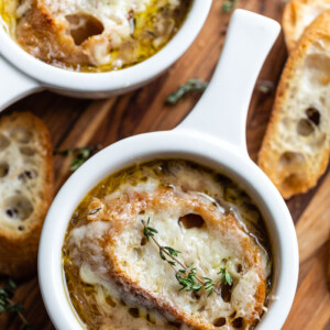 several bowls of french onion soup topped with bread, cheese, and fresh herbs