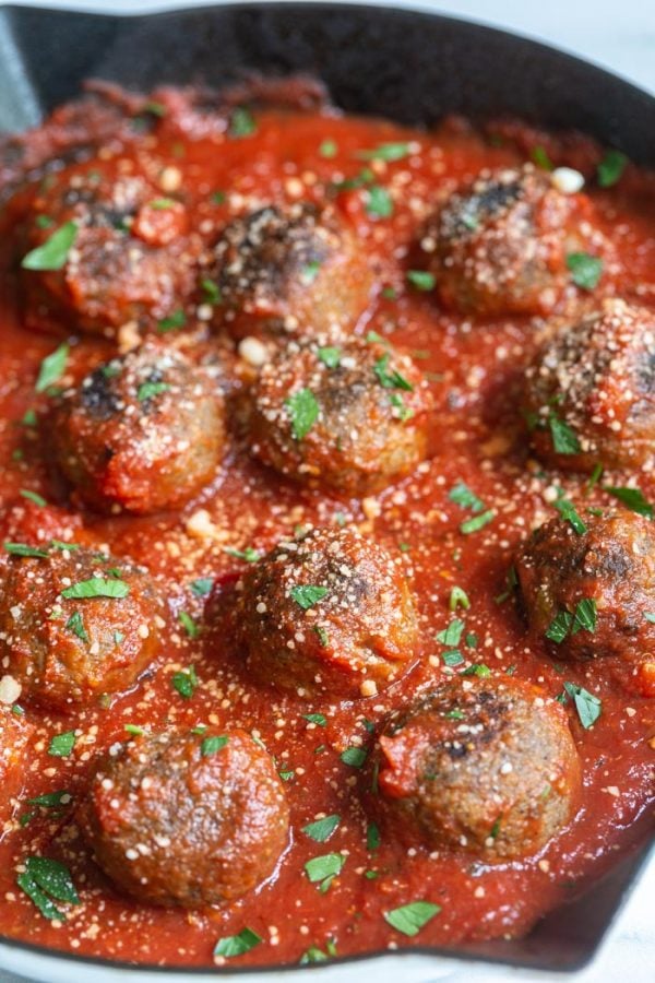 vegetarian meatballs in a skillet with tomato sauce and sprinkled with vegan cheese and parsley