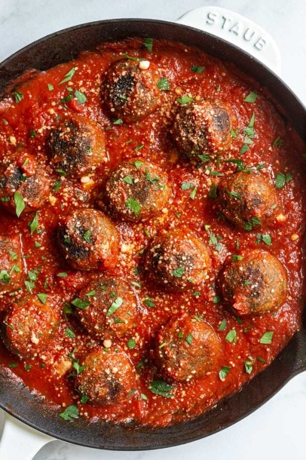 vegetarian meatballs in a skillet with tomato sauce and sprinkled with vegan cheese and parsley. vegan meatballs recipe