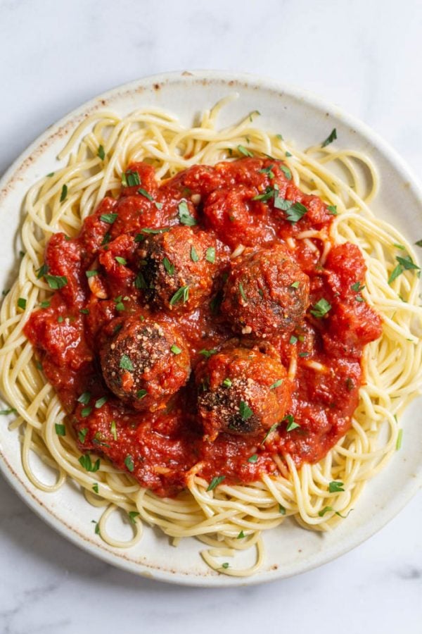 large plate filled with spaghetti that's topped with marinara sauce and 4 vegan meatballs and a sprinkle of parsley and vegan parmesan