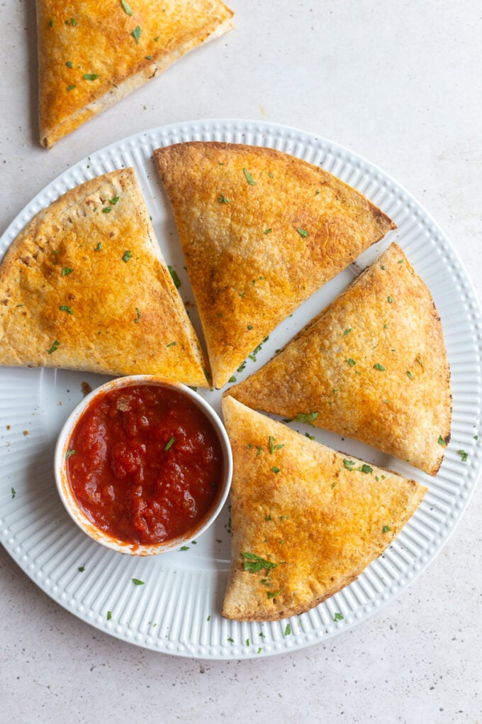 large pizza pockets made out of tortillas sitting on a plate with a cup of marinara on the side