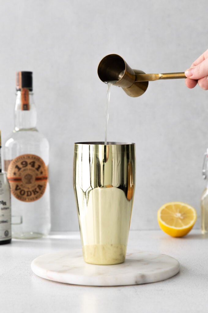 using a jigger to pour vodka into a cocktail shaker