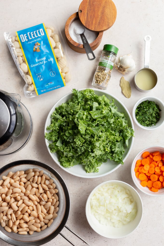 ingredients laid out for gnocchi soup: broth, gnocchi, kale, carrots, onions, beans, spices, salt and pepper